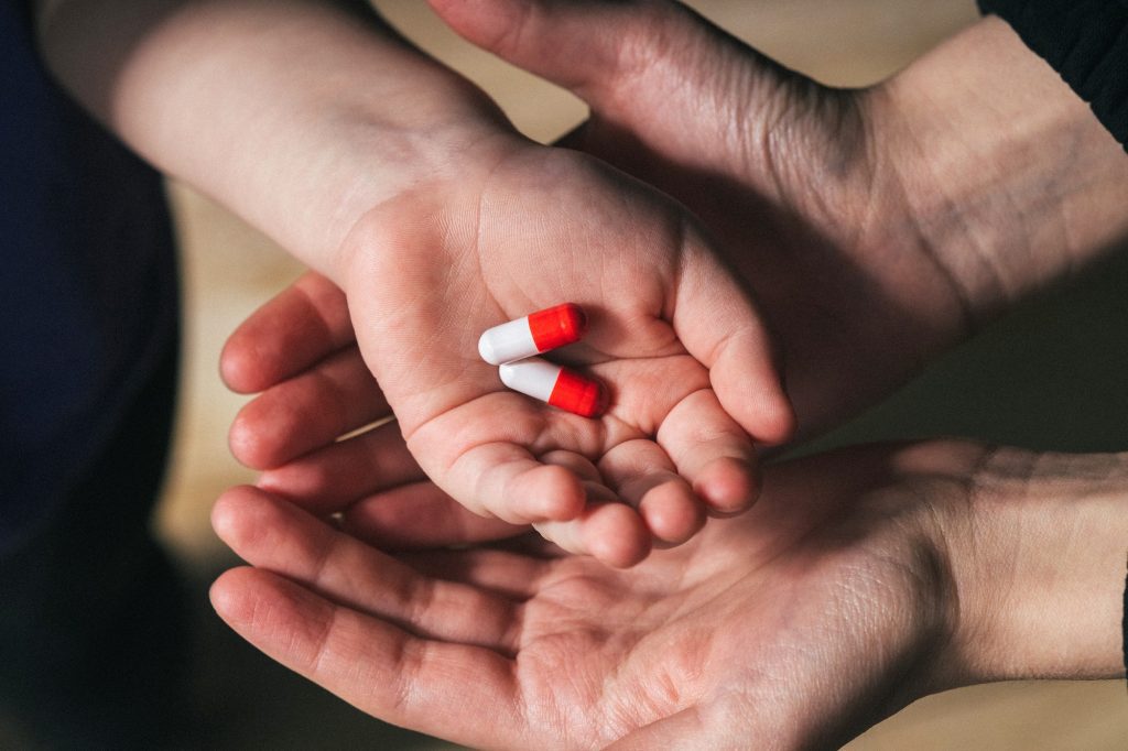 a woman gives a child pills or vitamins - hands with medicines close up in a low key