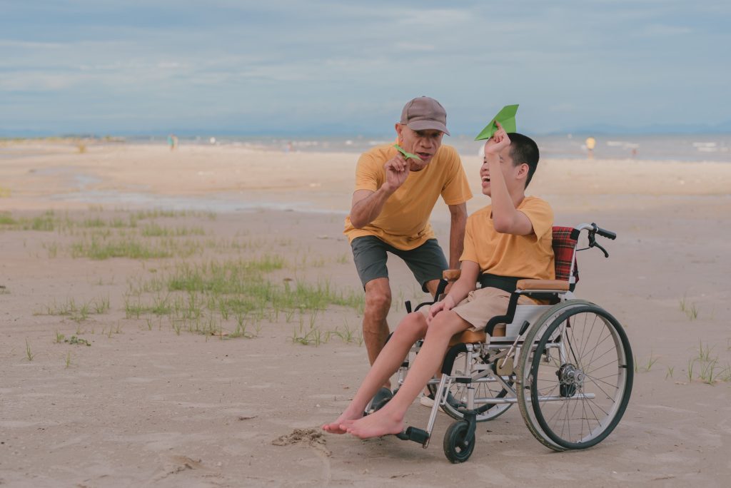 Young man with disability and parent or volunteer or caregiver relaxing on the sea beach.