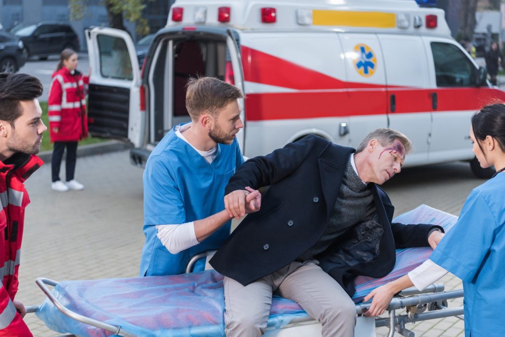 young paramedics helping injured man lie down on ambulance stretcher