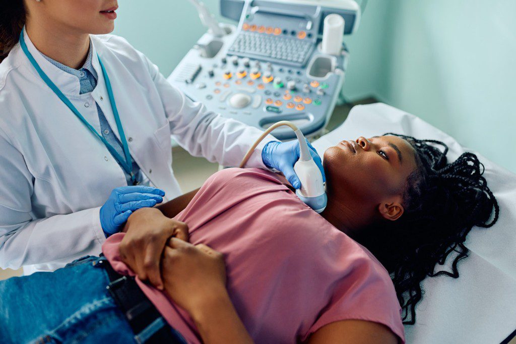 Black woman during ultrasound diagnostics of endocrine system and thyroid at medical clinic.