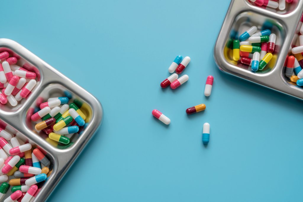 Multi-colored capsule pills in stainless steel tray and on blue background. Pharmacy banner.