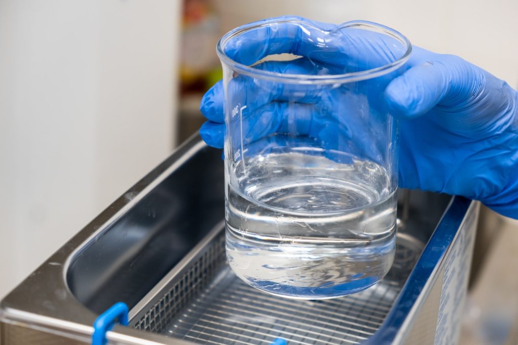 Scientist in blue rubber puts a beaker for dissolving or cleaning into an ultrasound bath. Clinical