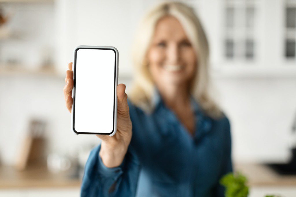 Smiling Mature Woman Showing Blank Smartphone, Advertising Mobile App For Grocery Delivery