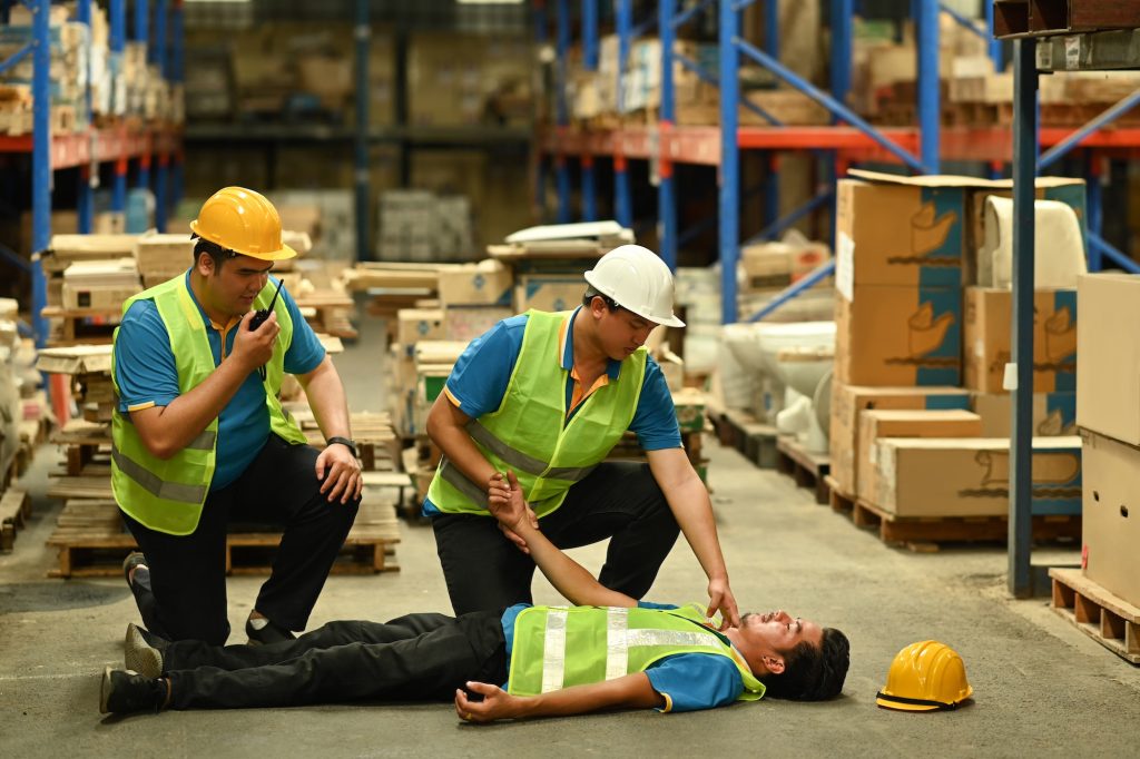 Shot of warehouse workers are helping and giving the injured first aid.
