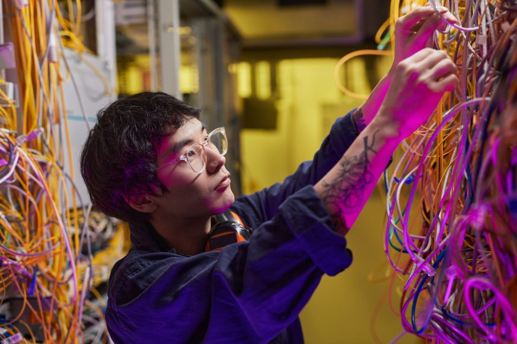 Young Technician Connecting Cables in Server Room