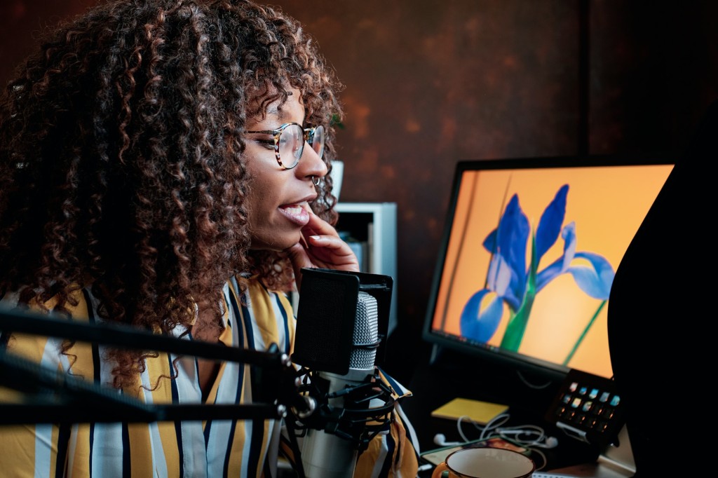 Afro female blogger speaking into a professional microphone while recording a podcast at home.