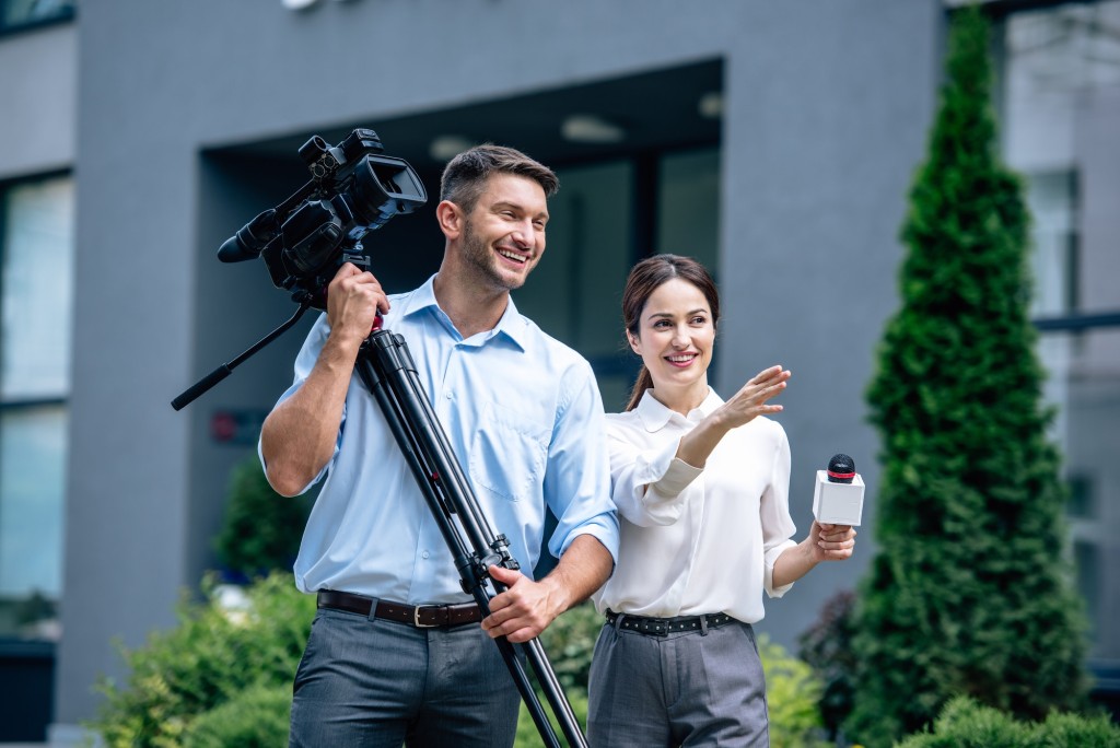 attractive journalist holding microphone and cameraman holding digital video camera