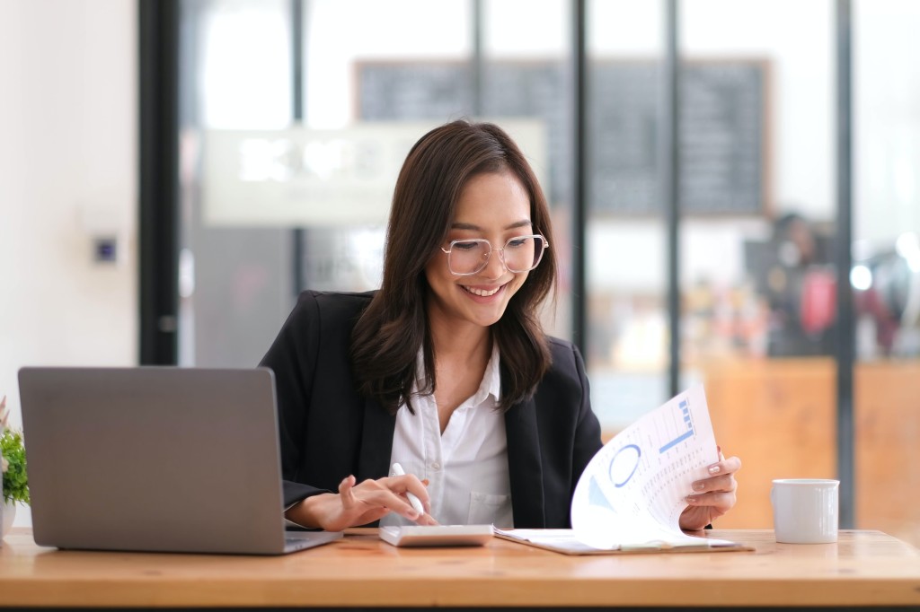 Beautiful Asian businesswoman analyzes charts using laptop calculator at the office.