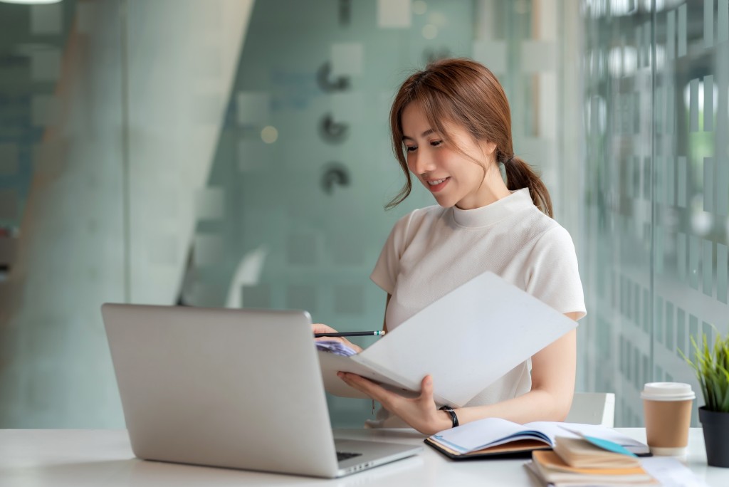 Beautiful Young Asian businesswoman holding documents to checking authenticity the laptop is placed