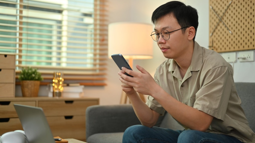 Image of adult asian man in casual watching video or playing game on smart phone