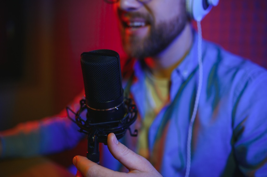 Male radio host with headphones on head and mic in studio reading news or broadcast show, toned