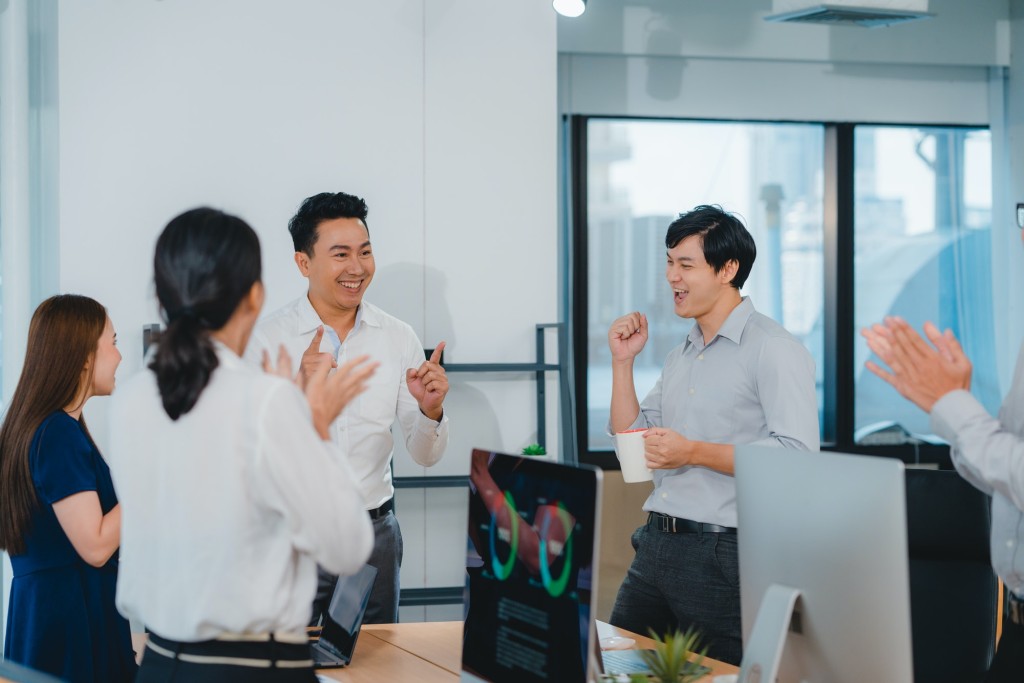 Group of young businesspeople celebrate giving five after dealing feeling happy in office.