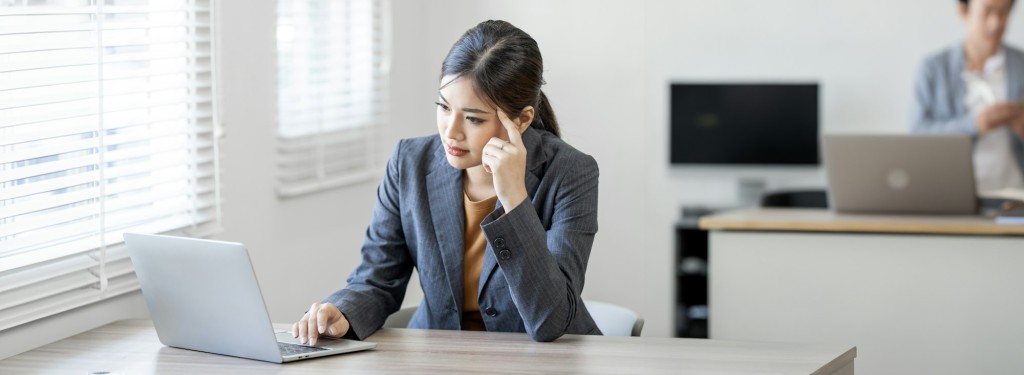 Thoughtful anxious asian business woman looking laptop screen and thinking solving problem at work