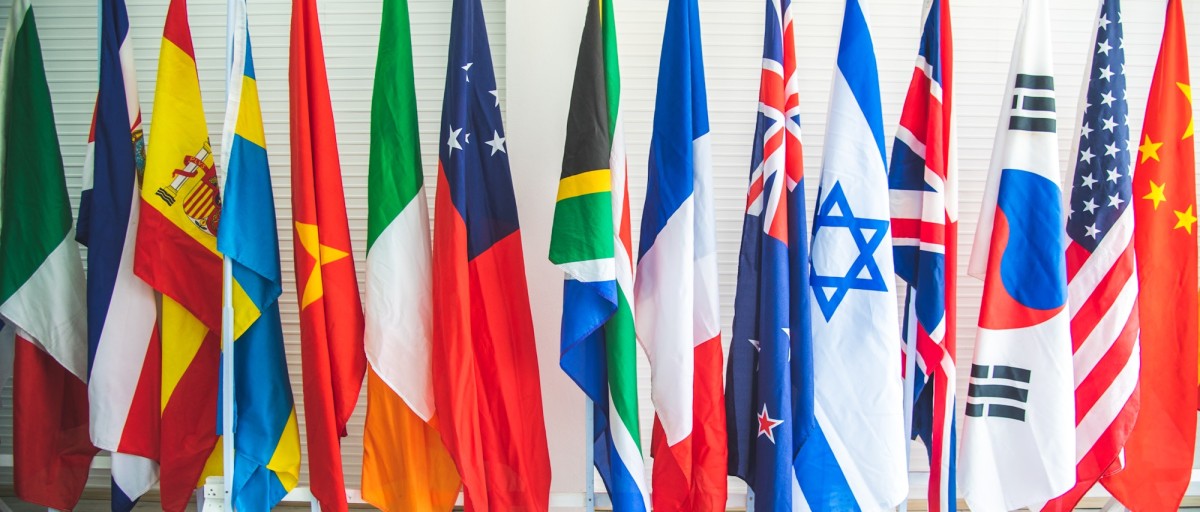collection of various flags of different countries standing tall together in a row on a stand