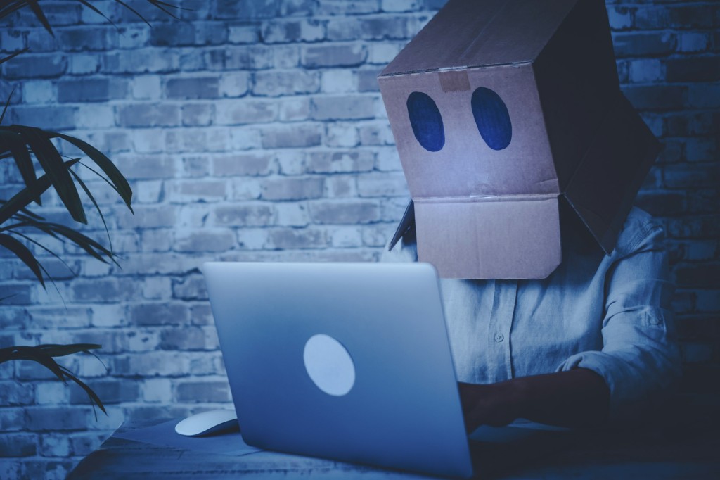 Anonymous hacker use laptop computer and connection at home wearing a box on his head