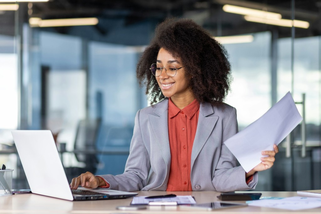 Confident businesswoman in modern office working on laptop holding documents