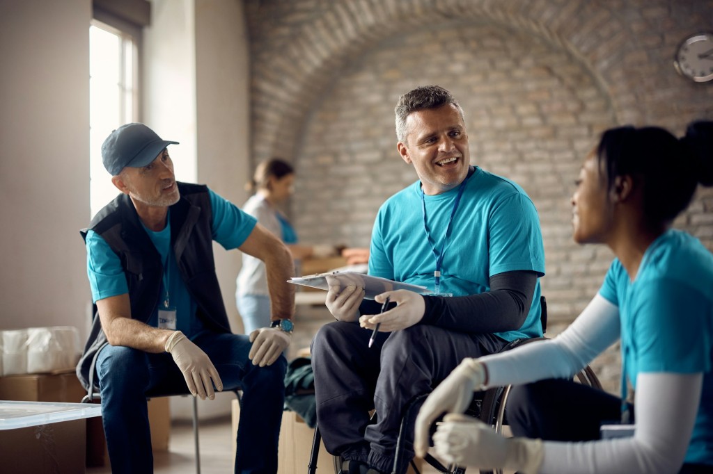 Happy coordinator in wheelchair having a meeting with volunteers at humanitarian aid center.