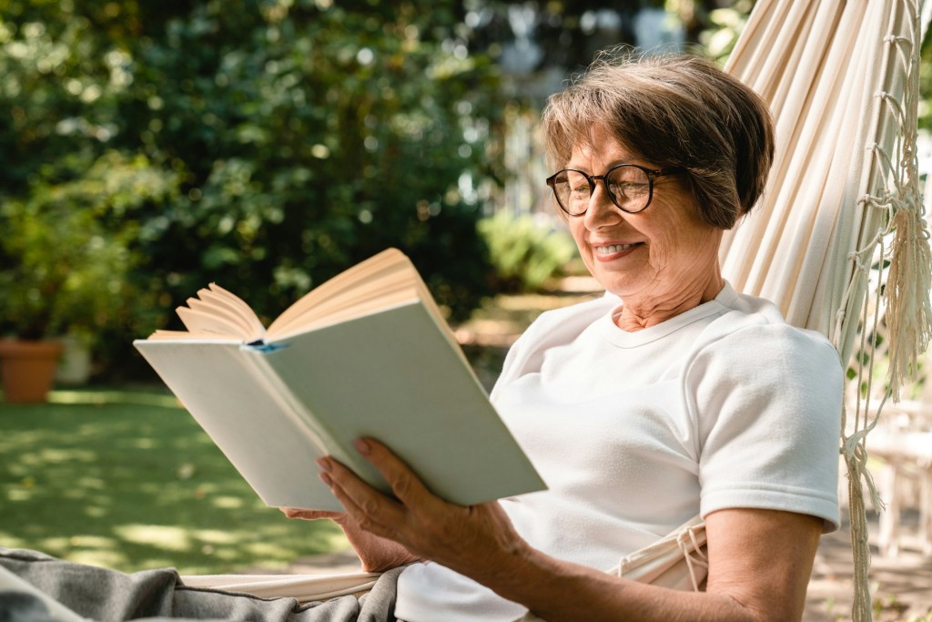 Happy relaxed old senior elderly woman grandmother relaxing while reading book in hammock