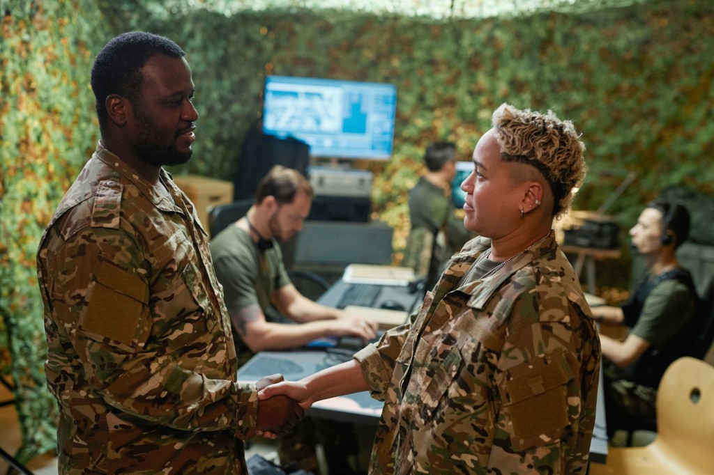 Two young intercultural officers in camouflage uniform shaking hands