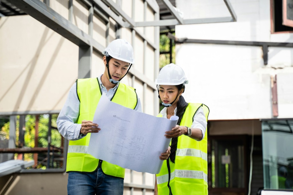 Asian colleague workers people wearing protective safety helmet and glasses onsite of architecture.